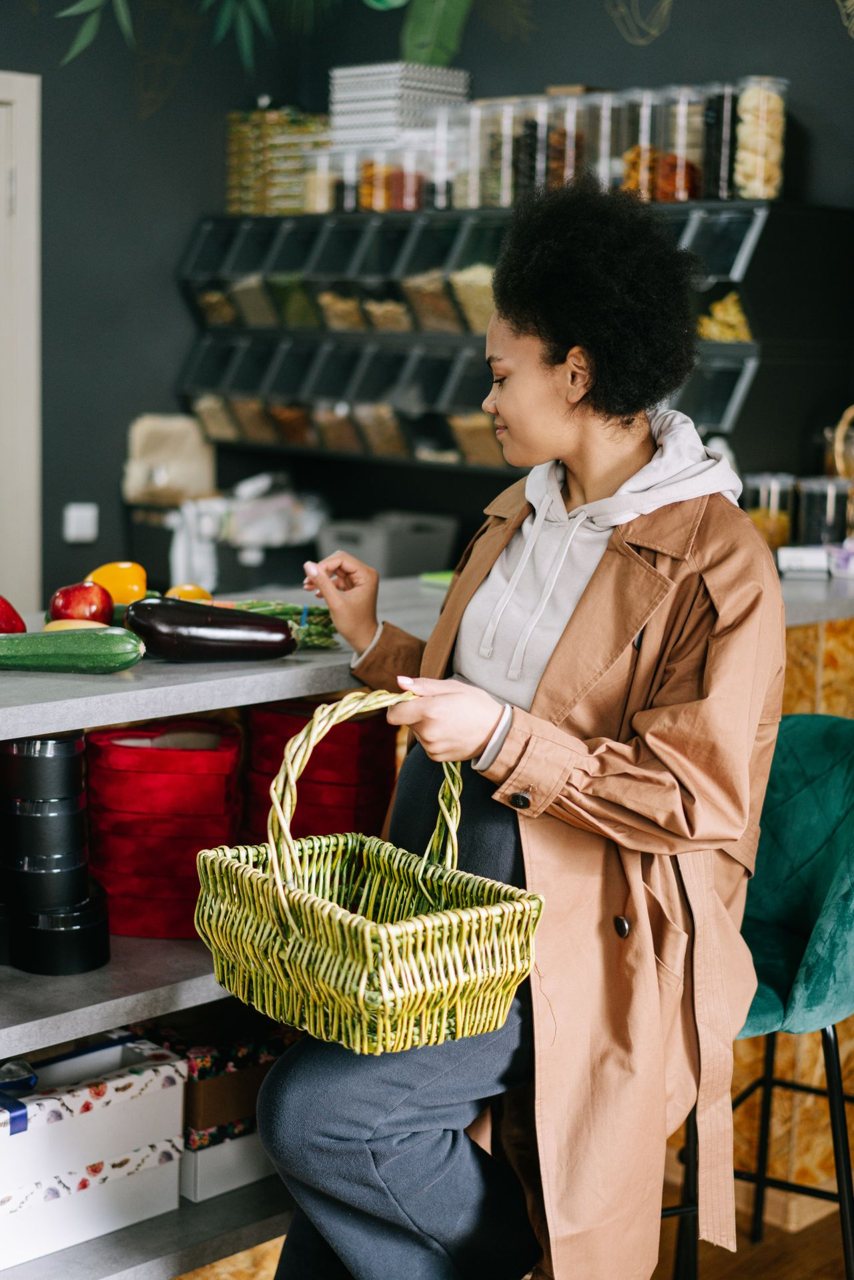 Free A woman with a basket selects fresh vegetables at a grocery store counter. Stock Photo
