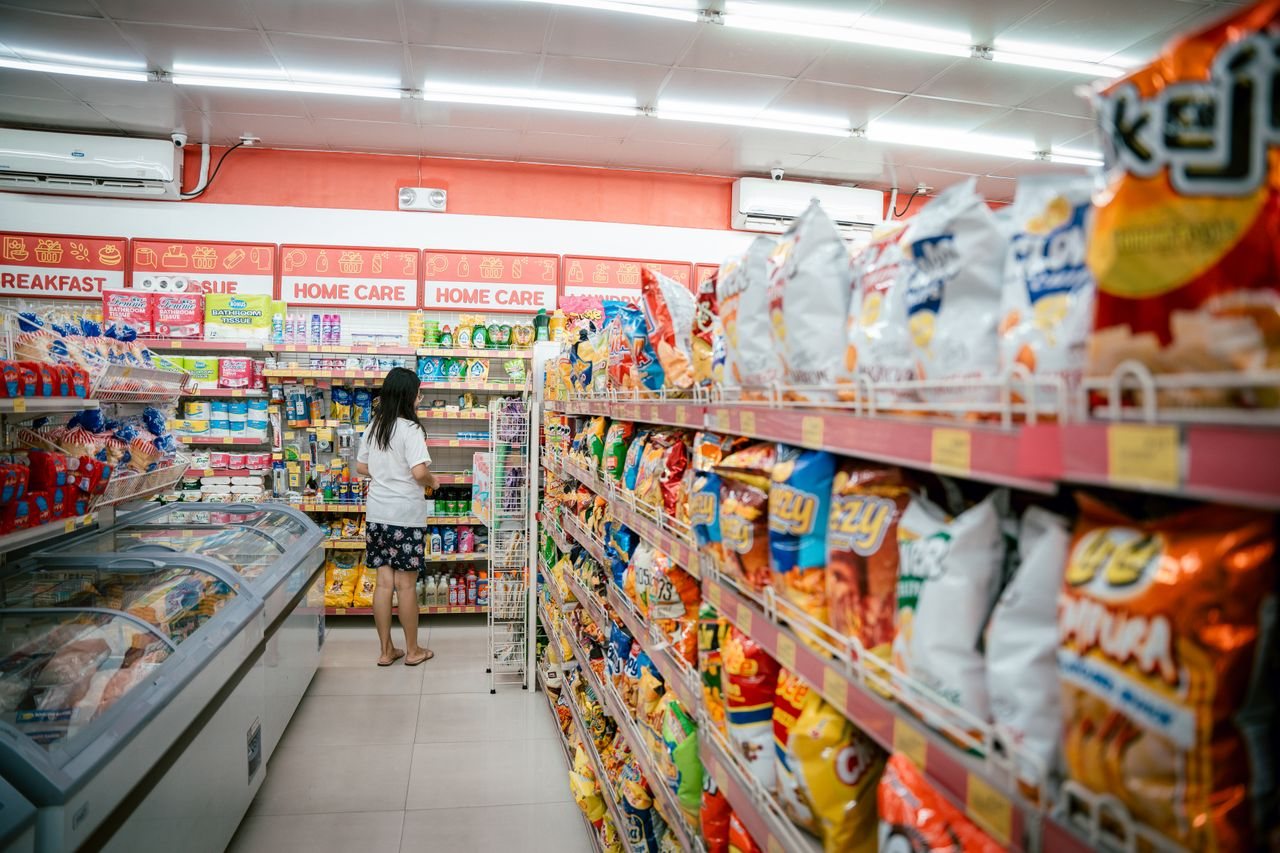 Free A woman browsing snack shelves at a supermarket, surrounded by various chips packages. Stock Photo