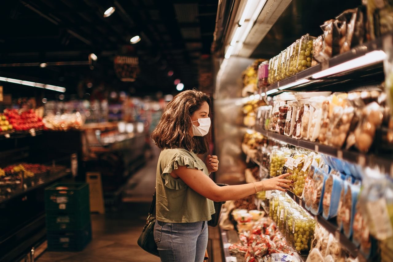 Free A woman wearing a mask shops for groceries in a supermarket aisle. Stock Photo